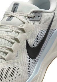 Gros plan d'une chaussure de course Nike blanche avec logo swoosh noir, empeigne en mesh et lacets de couleur claire passés dans des œillets en tissu.