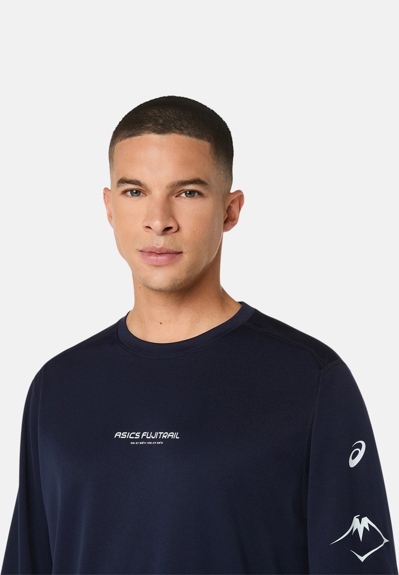 Chemise de sport à manches longues bleu marine avec logo blanc "ASICS FUJITRAIL", tissu texturé et graphique de montagne sur la manche droite.