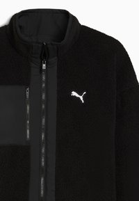 Sort fleece jakke med et glat stofstykke på venstre side og et hvidt Puma-logo. Har en høj krave og sorte lynlåse.