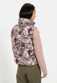Blomstret puffervest med høj krave, med et gråt, pink og grønt mønster. Strikænger i pink og lynlåslukning.