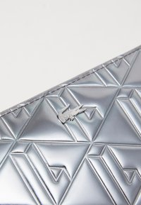 Portfel we wzór srebrny z geometrycznym designem, gładką teksturą i metalicznym akcentem w postaci logo krokodyla.