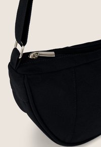 Borsa a spalla in tela nera con zip, caratterizzata da una forma curva e una superficie strutturata. Finiture metalliche per il fissaggio della tracolla.