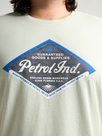 Lichtgroene katoenen T-shirt met een groot blauw en zwart grafisch label dat "Petrol Ind." weergeeft, met tekstdetails en een ontwerp in de vorm van een diamant.