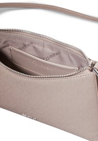 Kopertówka Calvin Klein na zamek w jasnym taupe z wzorem logo. Posiada gładką zewnętrzną powierzchnię i miękką wyściółkę wewnątrz, z akcentami srebrnej biżuterii.