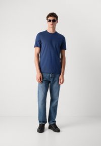 Camiseta de manga corta azul marino con cuello redondo, combinada con vaqueros de pierna recta azul claro y zapatillas negras. El modelo lleva gafas de sol.