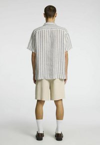 Camisa de manga corta a rayas en blanco y azul, combinada con pantalones cortos beiges. La camisa tiene un corte relajado y los pantalones cortos cuentan con un bolsillo trasero.