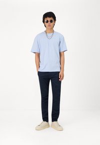 Camiseta de manga corta azul claro, pantalones navy y zapatillas crema. Incluye dos cadenas plateadas y gafas de sol redondas. Diseño simple y moderno.