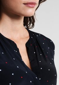Navy blouse with a subtle V-neck, featuring small embroidered stars in red and white, and soft, smooth fabric with a slightly draped design.