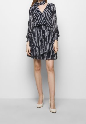 Woman wearing a black and white striped long-sleeve dress with ruffled skirt and cream pointed-toe heels, standing against a plain background.