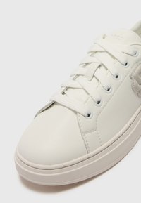 Sneaker bianca in pelle con punta rotonda, pannelli laterali texturizzati, lacci piatti bianchi e un branding sottile sulla tomaia, suola imbottita.
