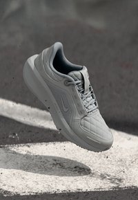 Scarpa da ginnastica grigia chiara con una texture trapuntata, lacci e logo Nike; suola in gomma dalla forma arrotondata.