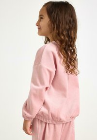 Różowy polarowy sweter z długimi rękawami, ściągaczami przy rękawach i u dołu. Miękka faktura, luźny krój, zestawiony z pasującymi spodniami.
