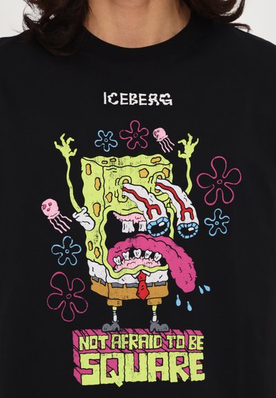 Black t-shirt featuring a colorful cartoon graphic of a square character with large eyes, tongue, and dripping details, with the text "NOT AFRAID TO BE SQUARE."