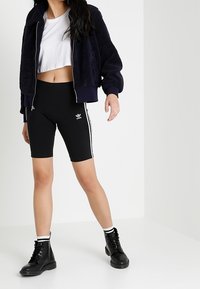 Black high-waisted bike shorts with white vertical stripes, paired with a cropped white t-shirt and a dark blue fuzzy bomber jacket. Black ankle boots.