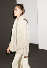 Lys beige oversized sweater kombineret med et flydende cremefarvet tørklæde og en skinnende satin cremefarvet nederdel, der har glatte teksturer og bløde draperinger.