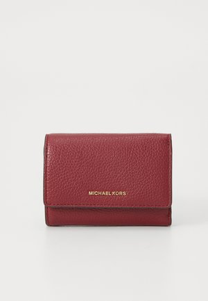 Kompakte, strukturierte rote Lederbörse mit goldenem "Michael Kors"-Logo auf der Vorderklappe, vor einem schlichten weißen Hintergrund präsentiert.