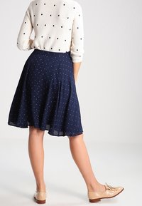 Laakere sininen polka dot -hame, jossa on leveä muotoilu ja joustava rakenne, yhdistettynä vaaleisiin loafereihin. Yllä on vaalea pusero, jossa on sinisiä pilkkuja.