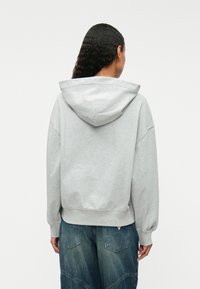 Γκρι φούτερ με κουκούλα και χαλαρή εφαρμογή, μαλακή υφή και ριμπ πέτο. Διαθέτει μεγάλη κουκούλα και χαμηλούς ώμους, συνδυασμένο με τζιν παντελόνι.