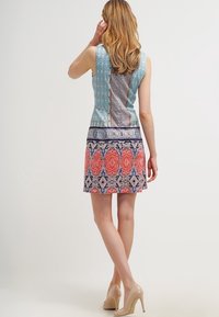 Šaty s potiskem, které mají přiléhavé tělo v modrých tónech a rozšířenou sukni se složitými červenými a růžovými vzory. Hladká látka bez rukávů.