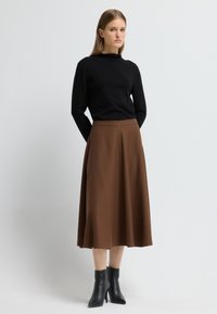 Camiseta negra de manga larga combinada con una falda corta en forma de A de color marrón. La falda presenta una tela texturizada, y el conjunto se completa con botas negras de tacón.