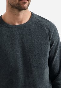 Donkergrijze gebreide trui met een ronde halslijn en een gestructureerde stof. Bevat raglanmouwen en een lichte ribbeling bij de kraag.