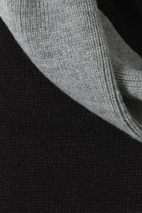 Grau gestrickter Stoff legt sich über einen strukturierten schwarzen Strickhintergrund und zeigt den Kontrast in Farbe und Material.
