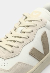 Hvite lær sneakers med beige semsket detaljer, med runde lisser, perforerte detaljer og en gjenkjennelig "V"-logo på siden.