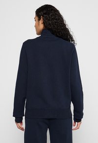 Pull-over bleu marine avec un col haut, des poignets côtelés et un ourlet côtelé. Fabriqué en tissu doux avec une texture lisse. Design simple sans motifs.