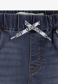 Pantalones de mezclilla azul marino con cintura elástica y cordón blanco con la marca "LEVI'S", costuras amarillas contrastantes y remaches de cobre.
