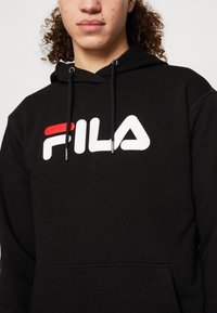 Felpa nera realizzata in un mix di cotone, con un prominente logo FILA bianco e rosso davanti, dotata di cordini e tasca a marsupio.