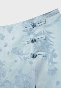 Tissu bleu clair avec des motifs floraux subtils, avec trois fermetures décoratives à boutons noués le long d'une couture verticale.