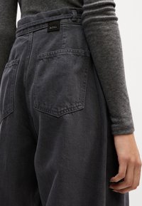 Pantalones de cintura alta en tejido de denim de color gris oscuro. Presenta una cinturilla plana con presillas para cinturón, dos bolsillos traseros y un branding sutil.