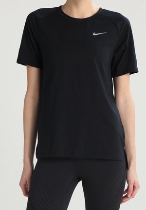 Personne portant un t-shirt Nike noir uni à manches courtes avec un petit logo Nike sur le haut gauche de la poitrine, assorti à des leggings noirs.