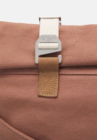 Bruine canvas tas met een gestructureerd oppervlak, met een afneembare stoffen schouderriem en een metalen sluiting. De leren accenten hebben een kruissteekdetail.
