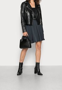 Svart skinnbikerjacka med silverdragkedjor, kombinerad med en mörkgrå utsvängd kjol. Svart texturerad handväska och ankelstövlar fullbordar looken.