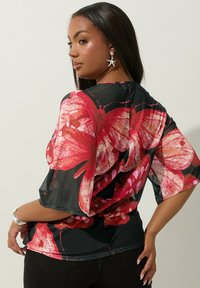 Musta läpinäkyvä paita, jossa on eläväinen vaaleanpunainen kukkakuosi, lyhyet, leveät hihat ja löysä istuvuus. Yksityiskohtana sileä tekstuuri.