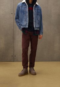 Jeansjacka med vit fuskpälskrage, lager på lager över en svart skjorta och rutigt flanell. Bruna kordflöjtbyxor och grå stövlar fulländar looken.