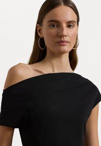 Black off-the-shoulder top with a smooth, matte texture. Features a wide neckline and short sleeves, highlighted by minimalistic design.