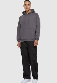 Sudadera gris con cordones, bolsillo frontal, combinada con pantalones cargo negros con múltiples bolsillos, llevados con zapatillas blancas.