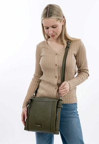 Borsa verde in pelle a tracolla con forma rettangolare, cinturino regolabile e chiusura magnetica frontale. Presenta un dettaglio logo discreto.