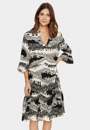 Schwarzes und weißes Blümchenmuster-Kleid mit V-Ausschnitt, schwingenden Ärmeln und gestuftem Rock. Hergestellt aus leichtem Stoff.