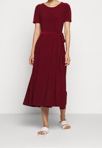 Burgunderröd knälång klänning med korta ärmar, rund halsringning och ett knytbart midjebälte; slätt tyg med plisserad kjoldetalj.