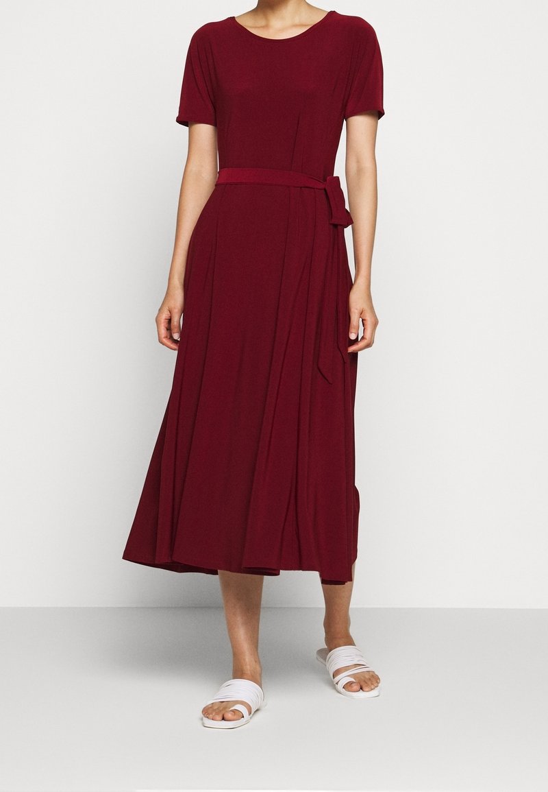 Burgunderröd knälång klänning med korta ärmar, rund halsringning och ett knytbart midjebälte; slätt tyg med plisserad kjoldetalj.
