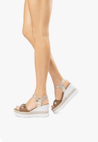 Brown and silver wedge sandals with a buckled ankle strap, textured white base, and woven midsole detailing. Open-toe design enhances breathability.