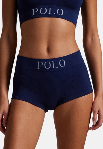 Set di reggiseno e short blu navy a costine con ampi elastici che mostrano la scritta "POLO" in grigio chiaro. Materiale con texture morbida, design aderente.