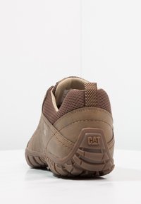 Braune Sneaker mit einem strukturierten Mesh- und Leder-Obermaterial, verstärkter Zehenkappe und Gummisohle mit einem Profilmuster. CAT-Logo an der Ferse.