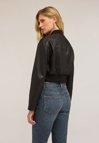 Czarna skórzana kurtka bomberka z prążkowanym kołnierzem, skróconym krojem i dopasowanymi rękawami. Noszona na wysokich niebieskich dżinsach z tylnymi kieszeniami.