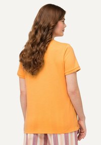 Camiseta corta de mangas en color naranja, hecha de algodón suave, con un corte relajado y un dobladillo recto. Mostrada desde la parte de atrás con cabello claro.