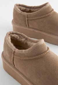 Bottines en daim marron avec une douce doublure en fourrure et une semelle plate-forme robuste. Présente des accents cousus et une silhouette arrondie.