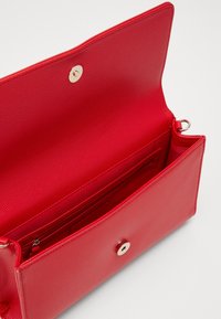 Červená texturovaná kůže uvnitř tašky s kovovým zlatým zapínáním na patentku, kapsou na zip a přihrádkami pro organizované uložení.